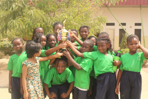 Gruppe von Kindern mit Pokal in einem Schulhof mit Bäumen und einem Gebäude im Hintergrund