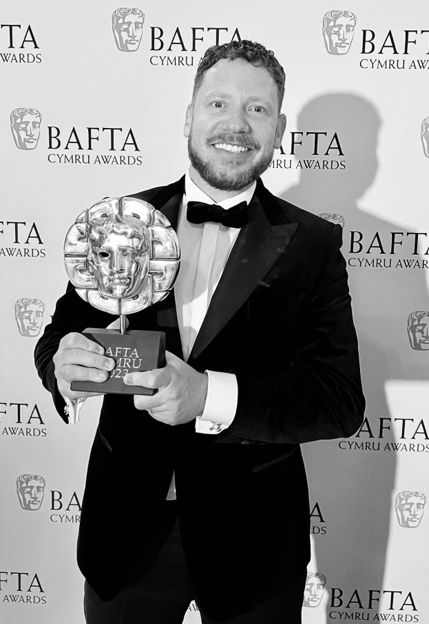 Ein Mann im Smoking hält einen BAFTA-Award, während er vor einer Tafel mit der Aufschrift "BAFTA Awards 2018" steht.