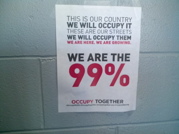 Schwarzes Plakat an einer Wand mit fetter Schrift, die "Occupy Wall Street" und "Wir sind die 99%." lautet.