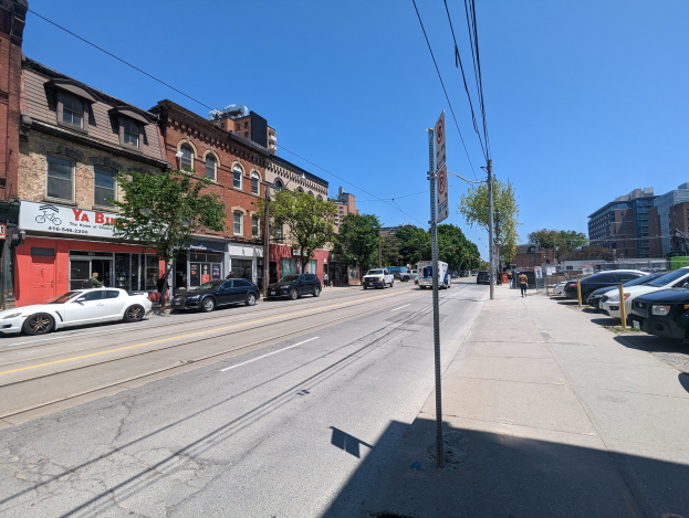 Stadtstraße mit parkenden Autos, Gebäuden, Bäumen, Strommasten und -drähten sowie einem Hintergrundschild "New York City Immobilien zum Verkauf".