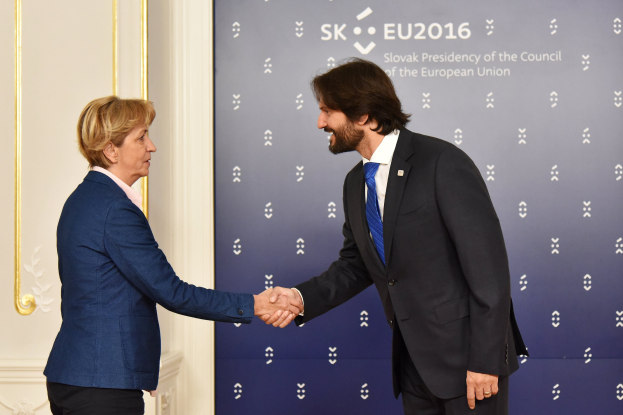 Bundeskanzlerin Angela Merkel und Bundeskanzler Joachim Gauck schütteln sich vor einer Wand mit einem 'EU-Gipfel'-Schild und einer Tür im Hintergrund die Hände, beide lächeln.