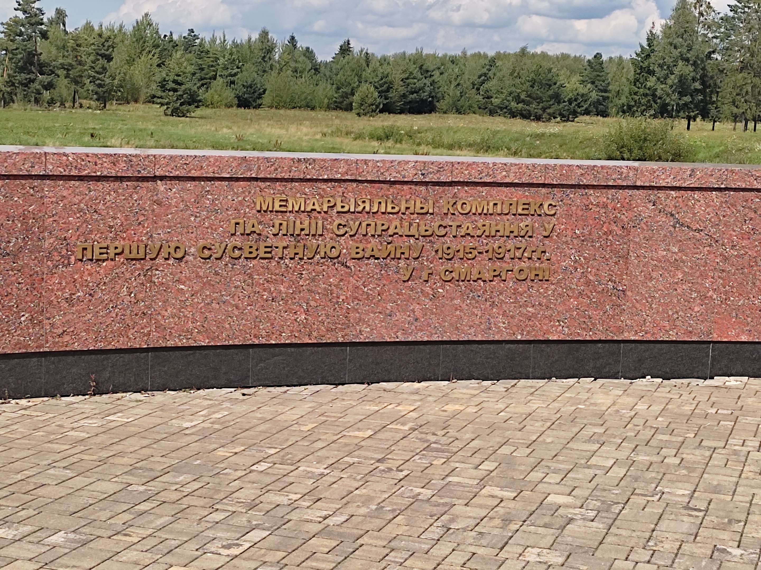 A brick-walkway leads to a monument with a wall inscribed "Memorial to the victims of the Soviet Union," set in a grassy park with trees under a cloudy sky.