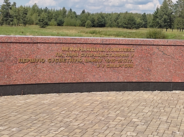 A brick-walkway leads to a monument with a wall inscribed "Memorial to the victims of the Soviet Union," set in a grassy park with trees under a cloudy sky.