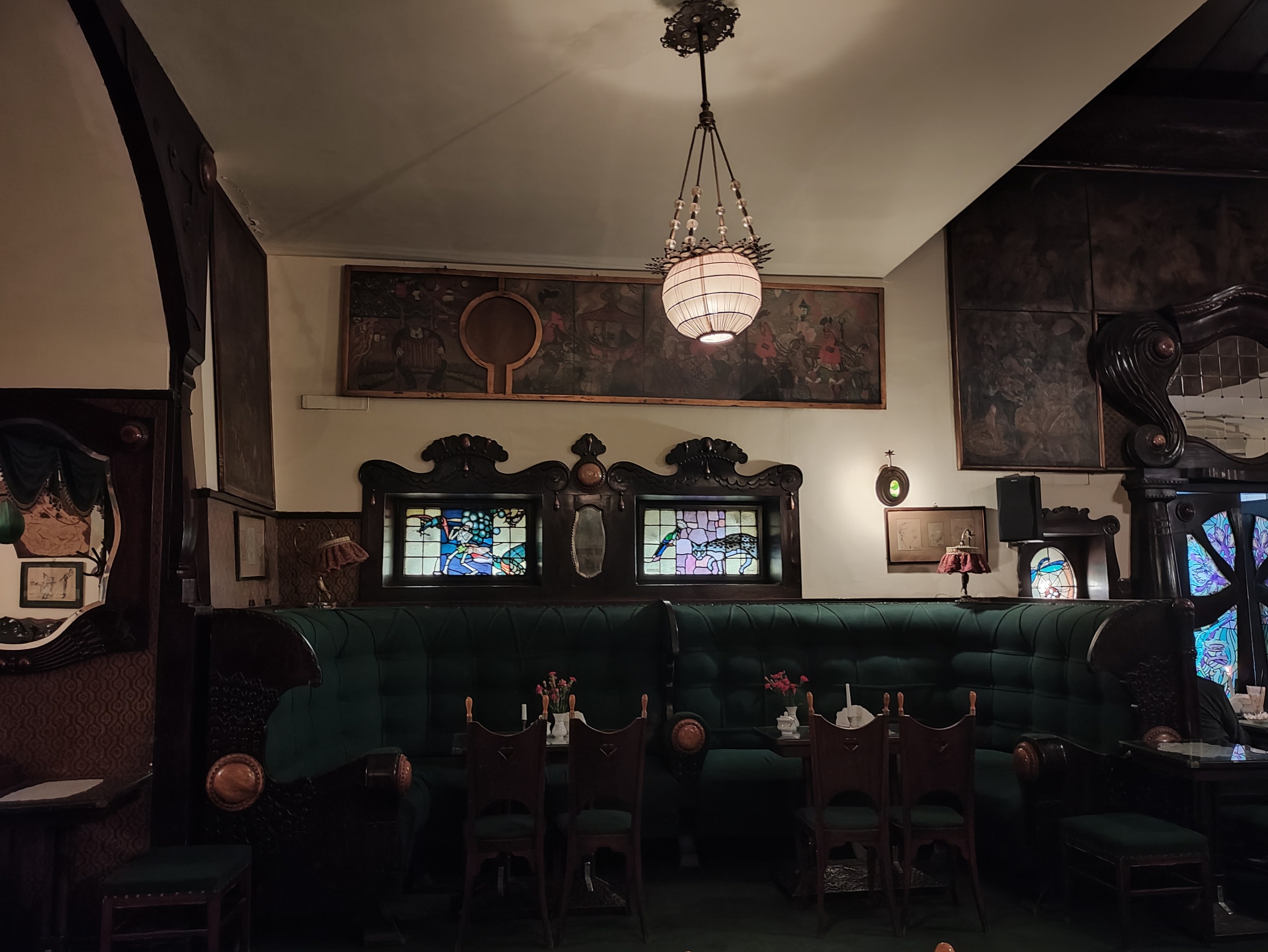 Innenraum eines gut eingerichteten Restaurants mit Tischen, Stühlen, Blumenvasen, Sofas, einem Kronleuchter, gerahmten Kunstwerken an den Wänden und einem Fenster auf der rechten Seite.