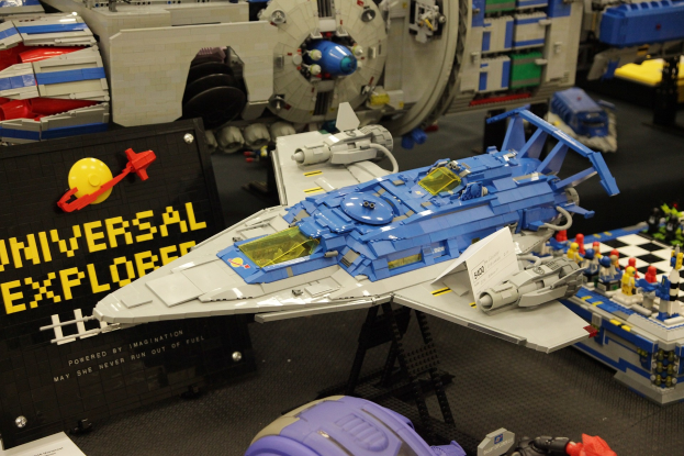 Lego-Modell eines Raumschiffs auf einer Ausstellung, umgeben von Spielzeugen und einer Tafel mit Text.