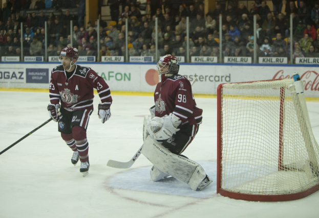 Zwei Eishockeyspieler in Helmen und Handschuhen konkurrieren auf einem Eisstadion mit einem Torpfosten und Zuschauern in den Rängen.