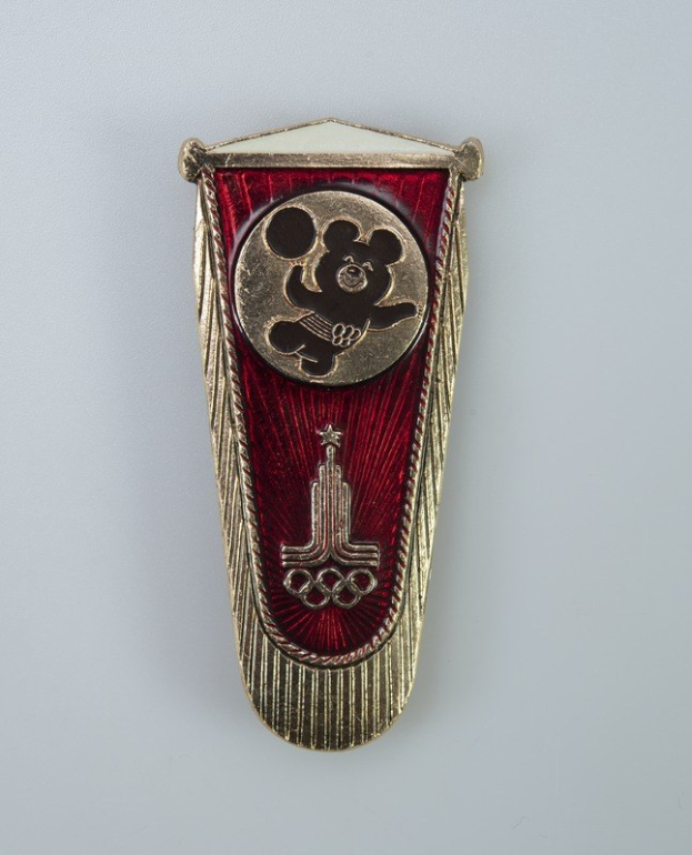 Roter und goldener Mickey-Maus-Anstecker im Buchmarken-Design mit goldener Umrandung und Mickey-Maus-Logo in der Mitte.