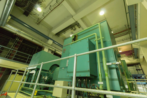 Großer industrieller Wärmetauscher in einem Gebäude, umgeben von Geländern, Rohren, Ventilen und Beleuchtungssystemen.