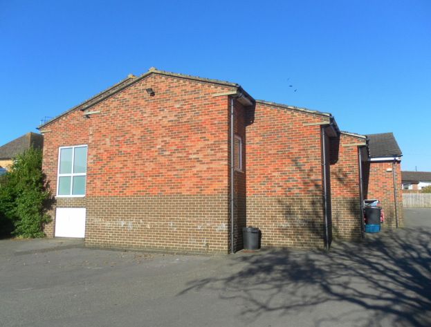 Red brick semi-detached bungalow with white door and windows, located on St Johns Road, St Johns Wood, Luton, surrounded by trees and dustbins.