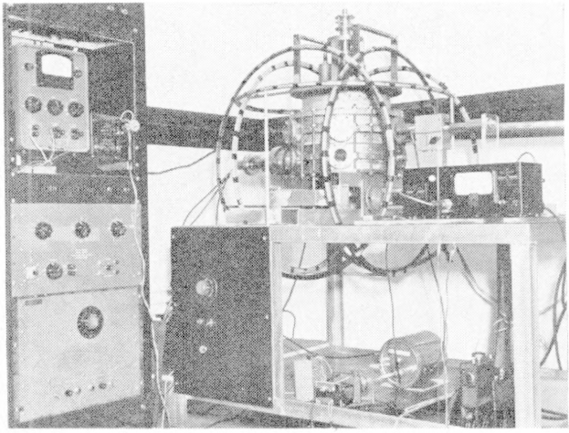 Schwarzes und weißes Foto einer Elektronenbeschleunigermaschine in einem Raum mit einer Wand im Hintergrund, mit Text unten.