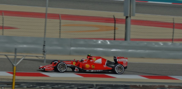 Ein rotes Ferrari Formel-1-Auto auf einer Rennstrecke, mit einem Fahrer im Cockpit, umgeben von einem Zaun und Reifen.