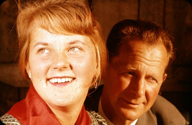 Zwei Menschen in inniger Umarmung, der Mann hat seinen Arm um die Taille der Frau gelegt und ihr Kopf ruht auf seiner Schulter, vor einer schlichten, ungeschmückten Wand.