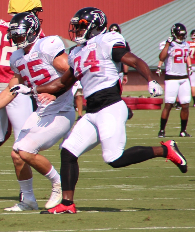 Eine Gruppe von Männern spielt Fußball auf einem Feld mit einer Wand im Hintergrund, alle tragen Helme und Fußballschuhe.