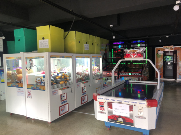 A room filled with various arcade games, featuring a game machine on the right, a visible floor, and ceiling lights.