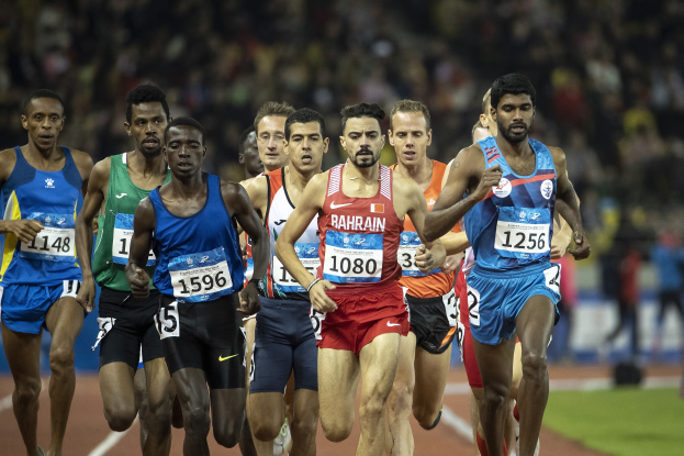 Eine Gruppe von Männern, die auf einer Laufbahn laufen und an einem Rennen teilnehmen, mit einigen, die zum Ziel sprinten, mit einem unscharfen Hintergrund.