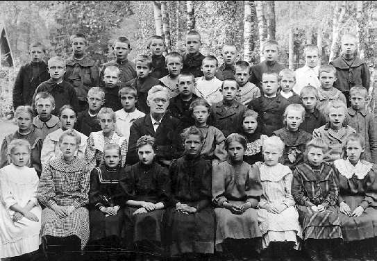 Schwarz-weißes Foto einer Gruppe von Kindern, die vor Bäumen posieren, mit dem Text "1930-1940 Russische Schule" unten.