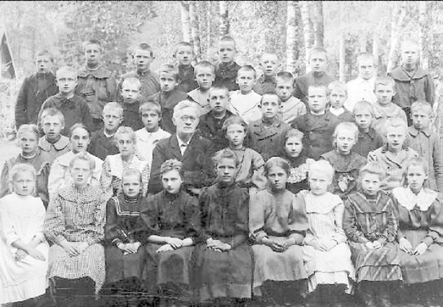 Schwarz-weißes Foto einer Gruppe von Kindern, die vor Bäumen posieren, mit dem Text "1930-1940 Russische Schule" unten.
