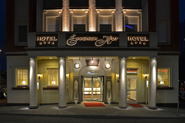 Das Essenerhof Hotel in Berlin, Deutschland, ein mehrstöckiges Gebäude mit Fenstern, Türen, Säulen und einer Namensschilder, das sich auf einer Straße mit Fahrzeugen auf der rechten Seite und einem klaren Himmel im Hintergrund befindet.