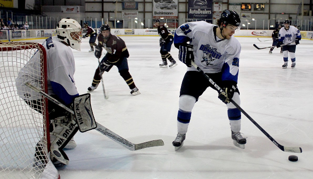 Gruppe junger Männer in Helmen und Eishockeyausrüstung, die auf einer Indoor-Eisfläche mit einem Torpfosten links und Wandbannern im Hintergrund Eis hockey spielen.
