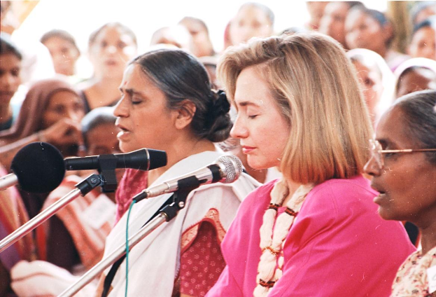 Zwei Frauen vor einem Publikum mit Mikrofonen, eine spricht, während die andere zuhört.