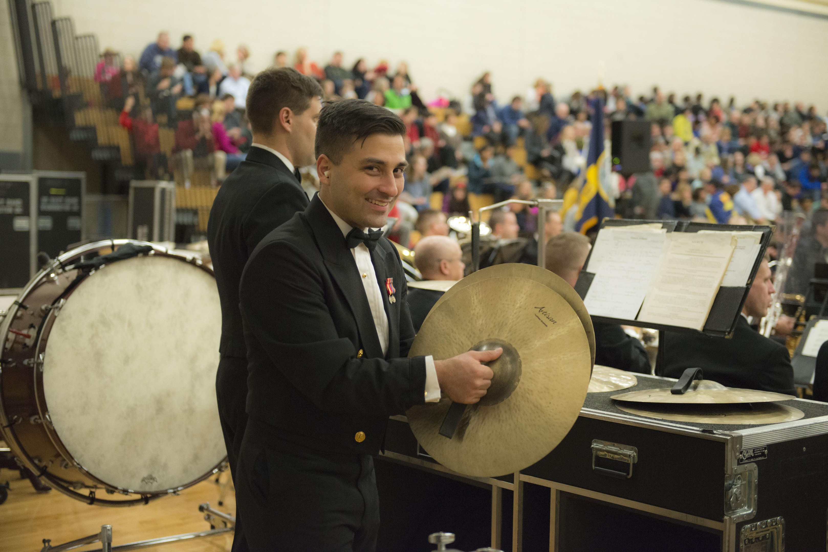 Eine Gruppe von Männern in Fracks, die auf der Bühne ein Schlagzeug und andere Instrumente spielen, mit Büchern auf Ständern und einer Wand im Hintergrund.