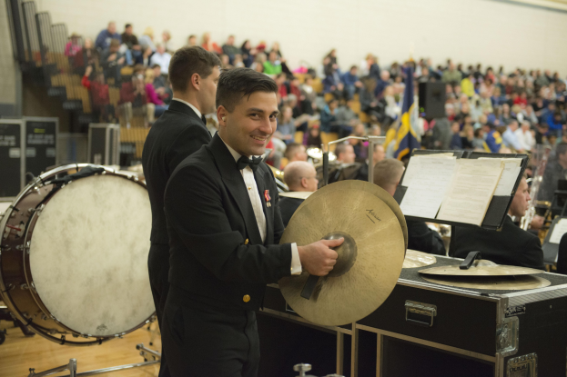 Eine Gruppe von Männern in Fracks, die auf der Bühne ein Schlagzeug und andere Instrumente spielen, mit Büchern auf Ständern und einer Wand im Hintergrund.