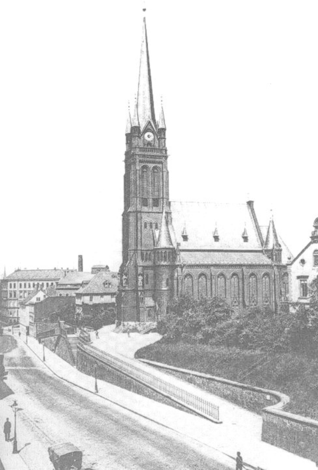 Schwarzes und weißes Foto einer Stadtstraße mit St. Peter Kirche im Hintergrund, gesäumt von Gebäuden, Bäumen, Fahrzeugen und Passanten.