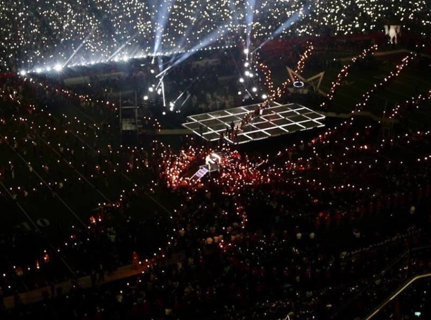 Eine große Menschenmenge in einem hell erleuchteten Stadion bei Nacht mit einem Performer auf der Bühne während der Olympischen Abschlussfeier.
