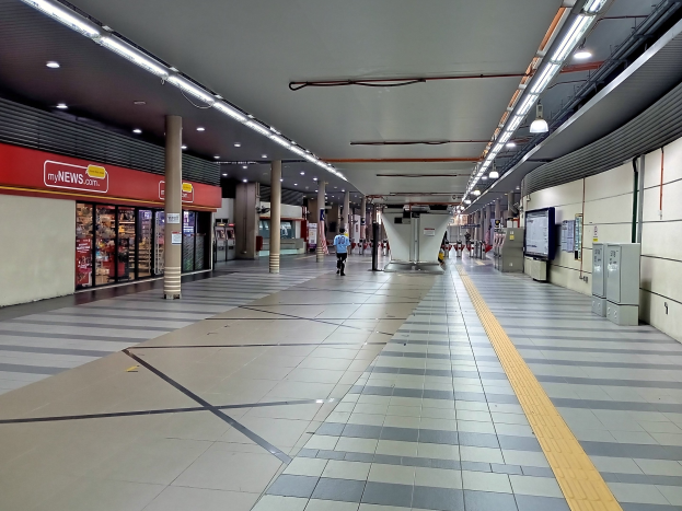 Leerer U-Bahnhof mit Menschen auf dem Boden, beleuchtet von Deckenlampen, Säulen und Geschäften auf der linken Seite und einem wandmontierten Fernseher.