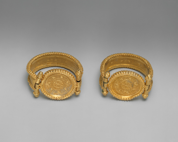 Goldarmbänder mit einem zentralen, kunstvoll gemusterten Medaillon, umgeben von kleineren runden Details, alles mit einem glänzenden Finish.