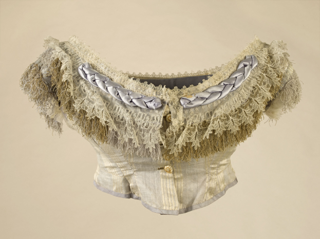 Ein weißer Korsett mit silberner Kragen und Fransen, das mit feiner Spitze verziert ist, vor einem cremefarbenen Hintergrund.