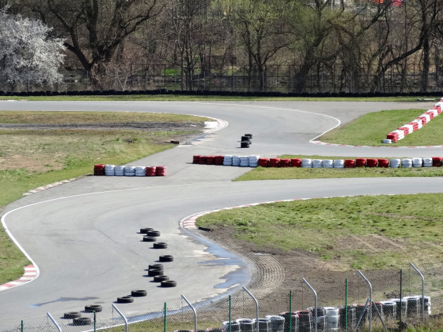 Rennstrecke voller Reifen, gesäumt von Gras und Maschendrahtzaun, mit Bäumen im malerischen Hintergrund.