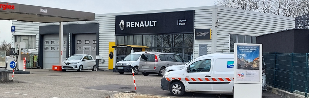 Ein Renault Autohaus mit parkenden Autos, einem Metallzaun, einer Texttafel, Pfosten, einem Schild, Bäumen und einem bewölkten Himmel.