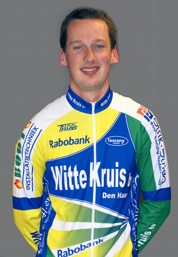 Ein männlicher Athlet posiert für ein Foto, trägt ein Shirt mit mehreren Sponsorenlogos.