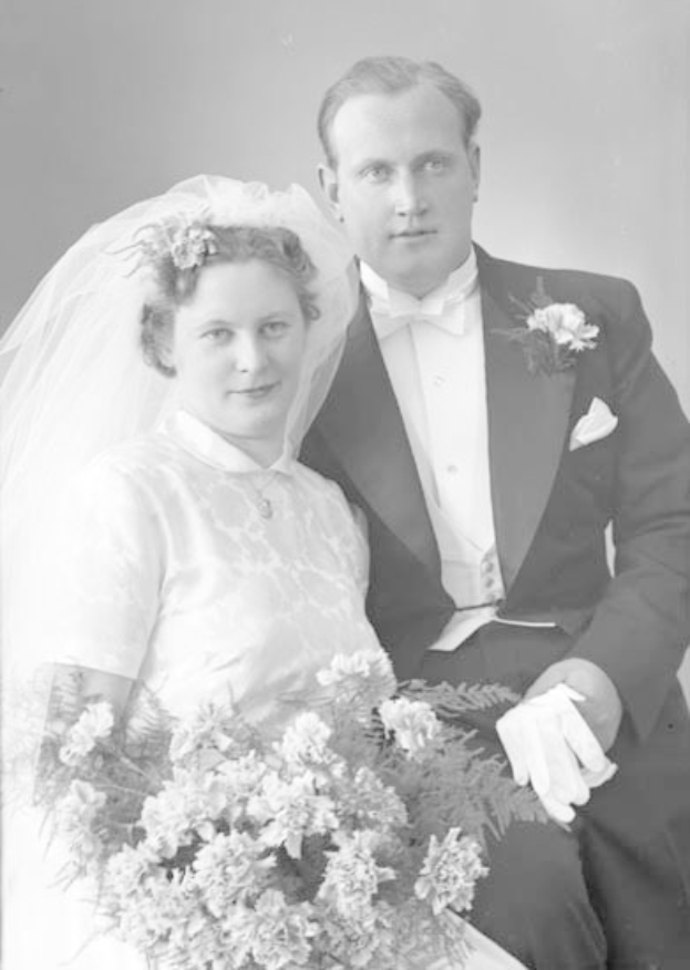 Schwarz-weißes Hochzeitsfoto eines grinsenden Mannes in einem Anzug und einer Frau mit einem Strauß, die sich verliebt anschauen.