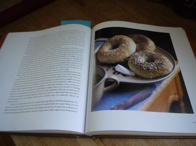 Ein aufgeschlagenes Buch auf einem Holztisch, mit Text auf der linken Seite und Donuts auf einem Teller mit einer Tasse auf der rechten Seite.