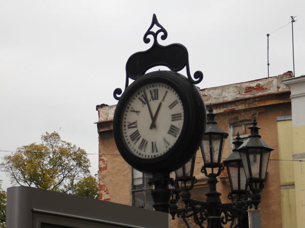 Uhr an der Seite eines Gebäudes montiert, beleuchtet von Straßenlaternen, mit Bäumen und anderen Gebäuden im Hintergrund.