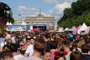Eine große Menschenmenge steht vor dem Brandenburger Tor in Berlin, Deutschland, viele tragen Mützen und Schutzbrillen, Zelte und Luftballons sind über das Gebiet verstreut, auf der linken Seite eine Bühne mit Lautsprechern und einem Bildschirm, sowie Bäume, Gebäude und ein bewölkter Himmel im Hintergrund.