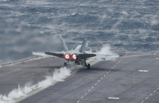 Ein Kampfflugzeug startet von einem Flugzeugträger auf dem Meer, wobei es Rauch hinterlässt.
