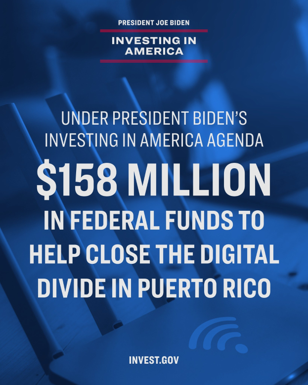 Ein Plakat mit Text über das Investing in America Agenda des Präsidenten Biden und 158 Millionen Bundesmittel für die digitale Kluft in Puerto Rico, mit einem Laptop, einem Stapel Papiere und einem Kaffeebecher auf einem Tisch davor.