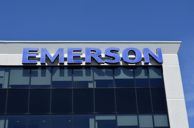 Emerson-Logo auf einer Gebäudefassade mit dem Text "Emerson investiert 1,5 Milliarden USD in den USA", unter einem klaren blauen Himmel.