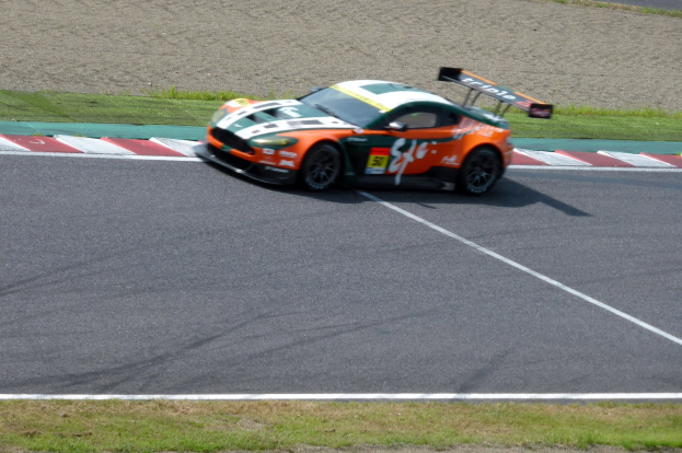 Aston Martin V12 Vantage GT3 Rennwagen auf einer Rennstrecke mit grüner Wiese.