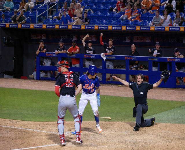 Baseballspieler rutscht ins Home Plate mit Zuschauern, Schildern, Metallpfosten und einer Decke mit Deckenlampen im Hintergrund.