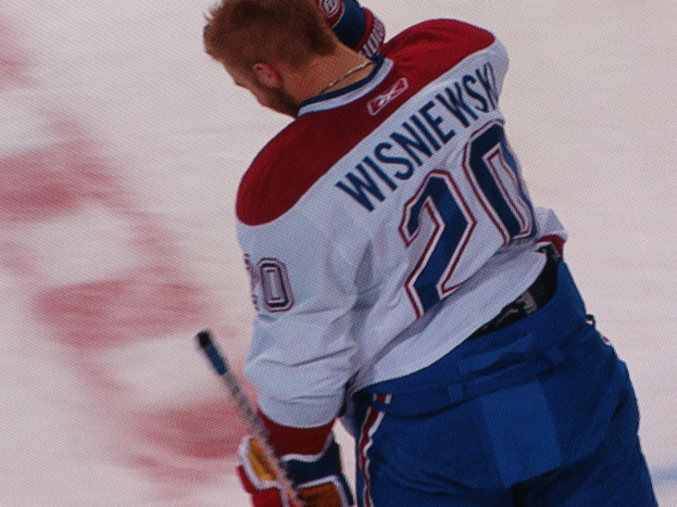 Professioneller Eishockeyspieler in einem 'Wisniewski'-Trikot, der einen Hockey-Schläger auf dem Eis hält und konzentriert schaut.