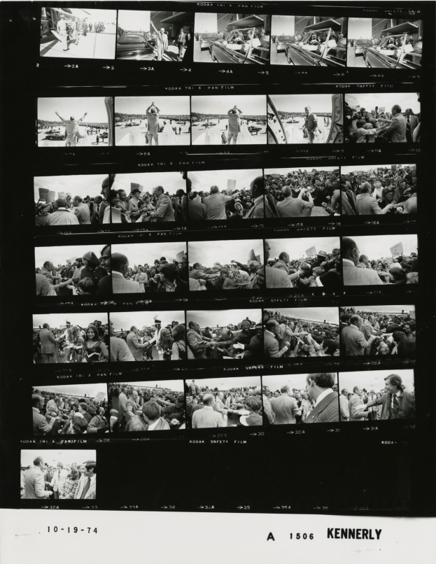 Schwarzes und weißes Foto einer vielseitigen Menge, die auf einen Fernsehbildschirm schaut und Text am unteren Rand hat.