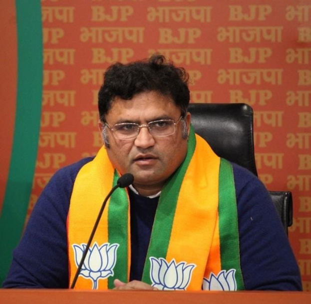 BJP-Führer Sanjay Kumar Reddy spricht auf einer Pressekonferenz in Neu Delhi, trägt eine Brille und einen Schal, mit einem Mikrofon auf dem Tisch und einem Banner im Hintergrund.