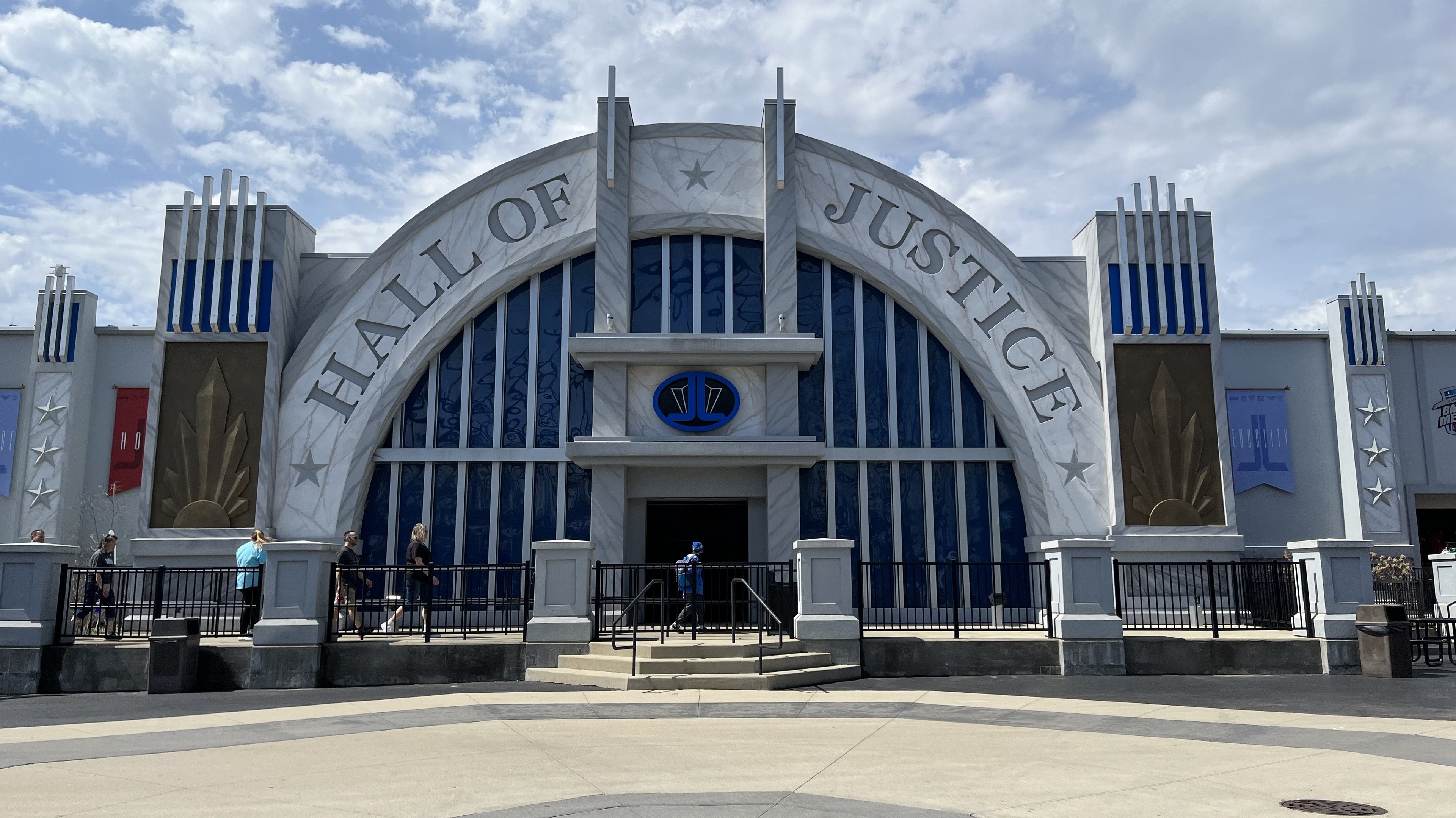 Entrance to the Hall of Justice at Disney's Hollywood Studios with a group of people standing in front, text and banners on the building, cloudy sky.