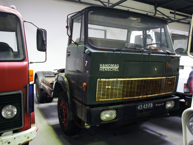 Eine Gruppe von Lkw, die nebeneinander in einer Garage geparkt sind, mit einer Wand und Metallstangen im Hintergrund, darunter ein Freightliner-Lkw.
