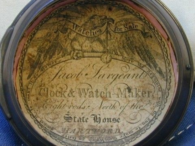 Nahaufnahme einer Taschenuhr mit eingraviertem Text und einem Bild auf einem blauen Tuch.