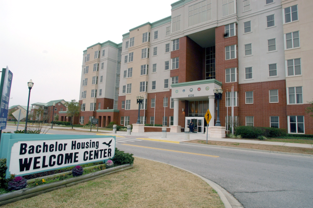 Außenansicht eines Bachelor Housing Welcome Centers mit Gebäuden, Straßeninfrastruktur, Fahrzeugen, Grünflächen und einem klaren Himmel.